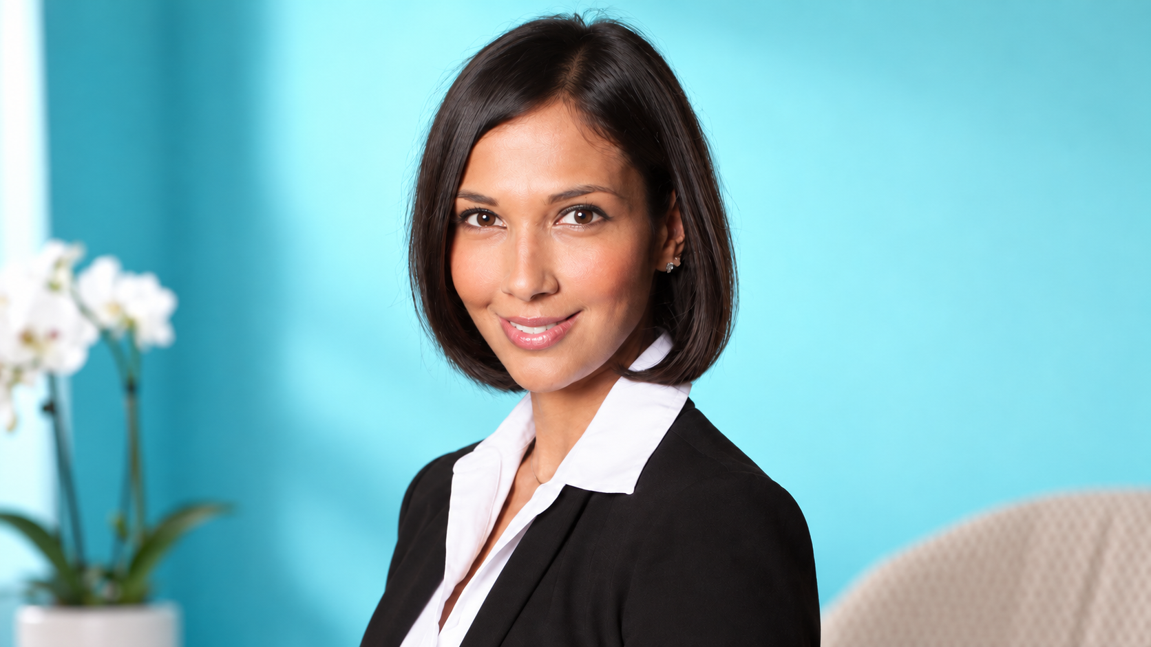 Feliza Castro, founder of The Healing Clinic, against a turquoise backdrop with a white orchid